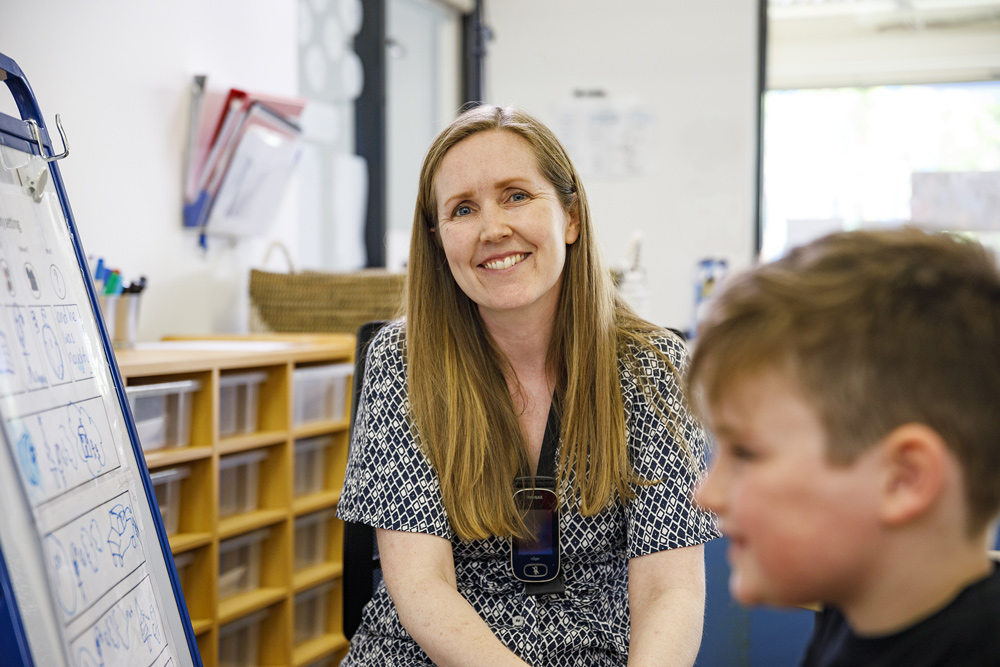 A child drawing on a whiteboard with a teacher.