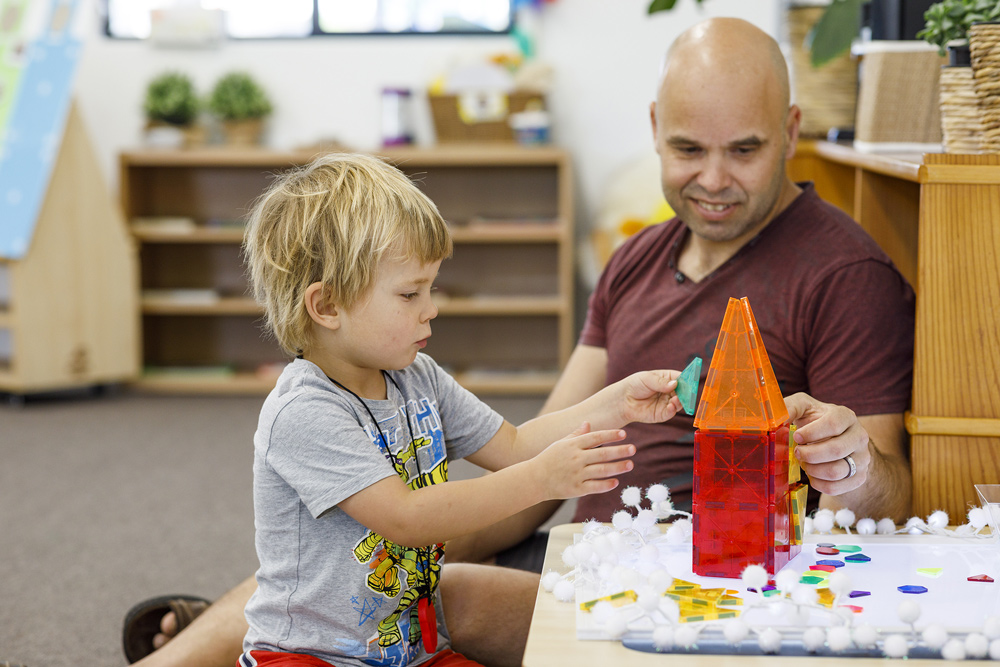 A child building a toy building out of blocks with his dad.