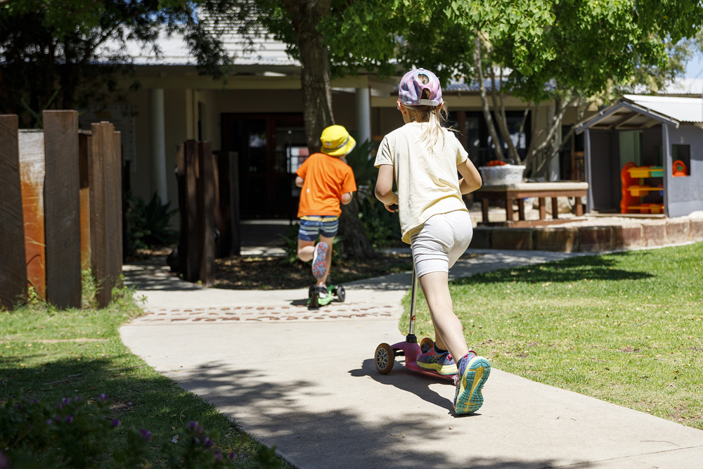 Two children riding scooter at TSH school.