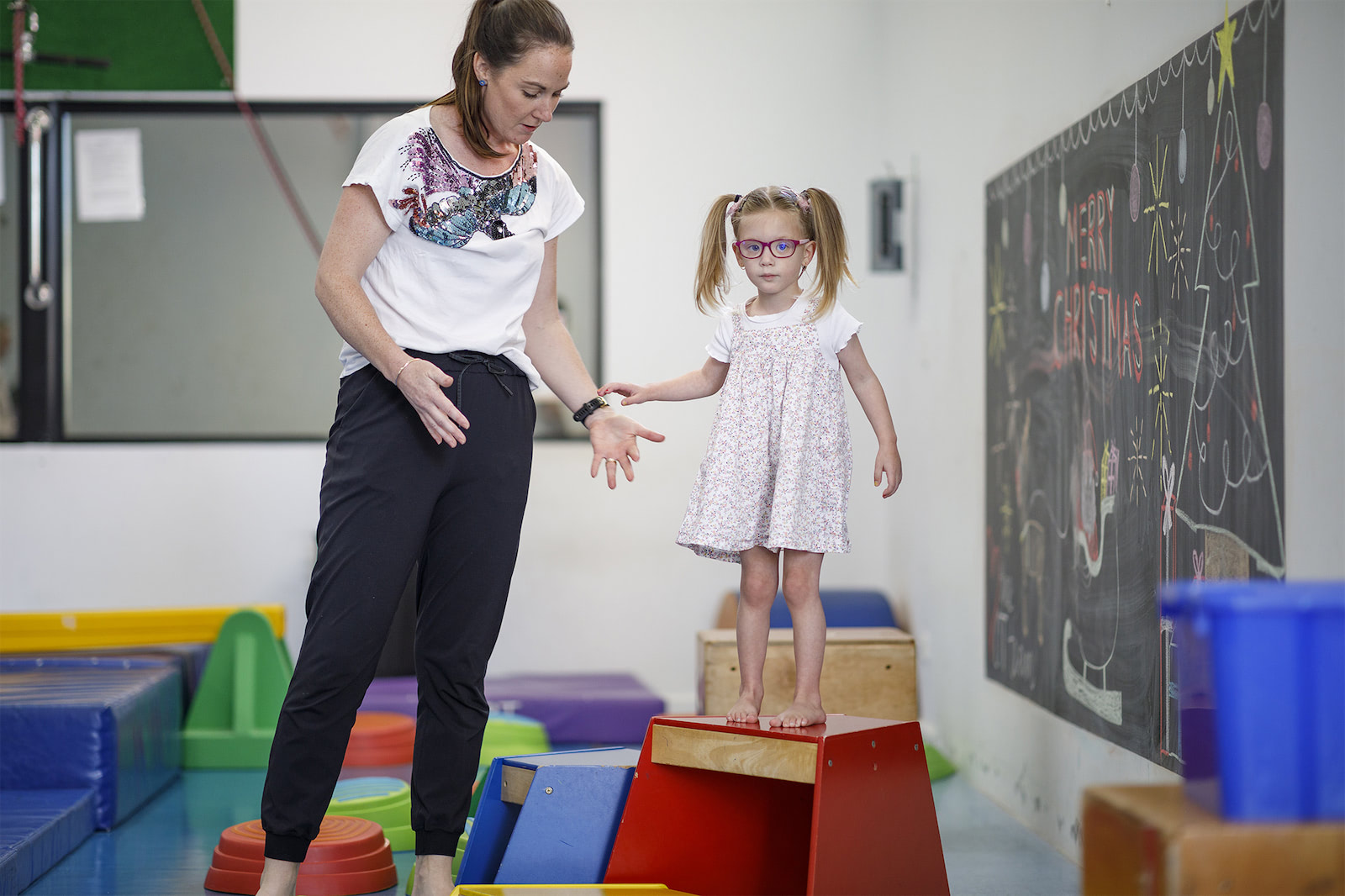 A child and therapist on a wooden block at a gymnasium.