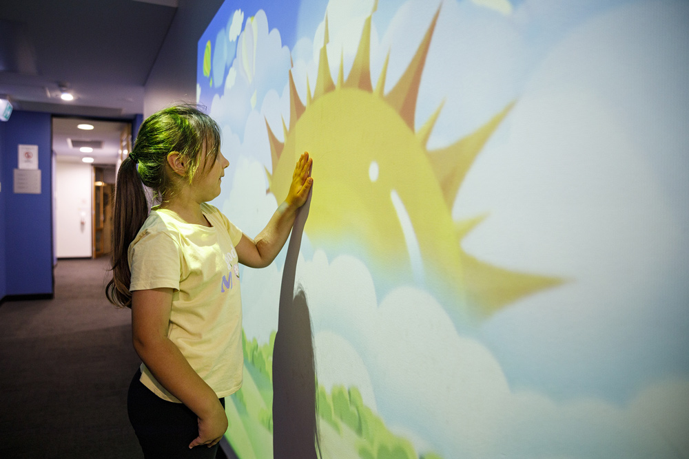 A child touching a wall with a cartoon sun painting.